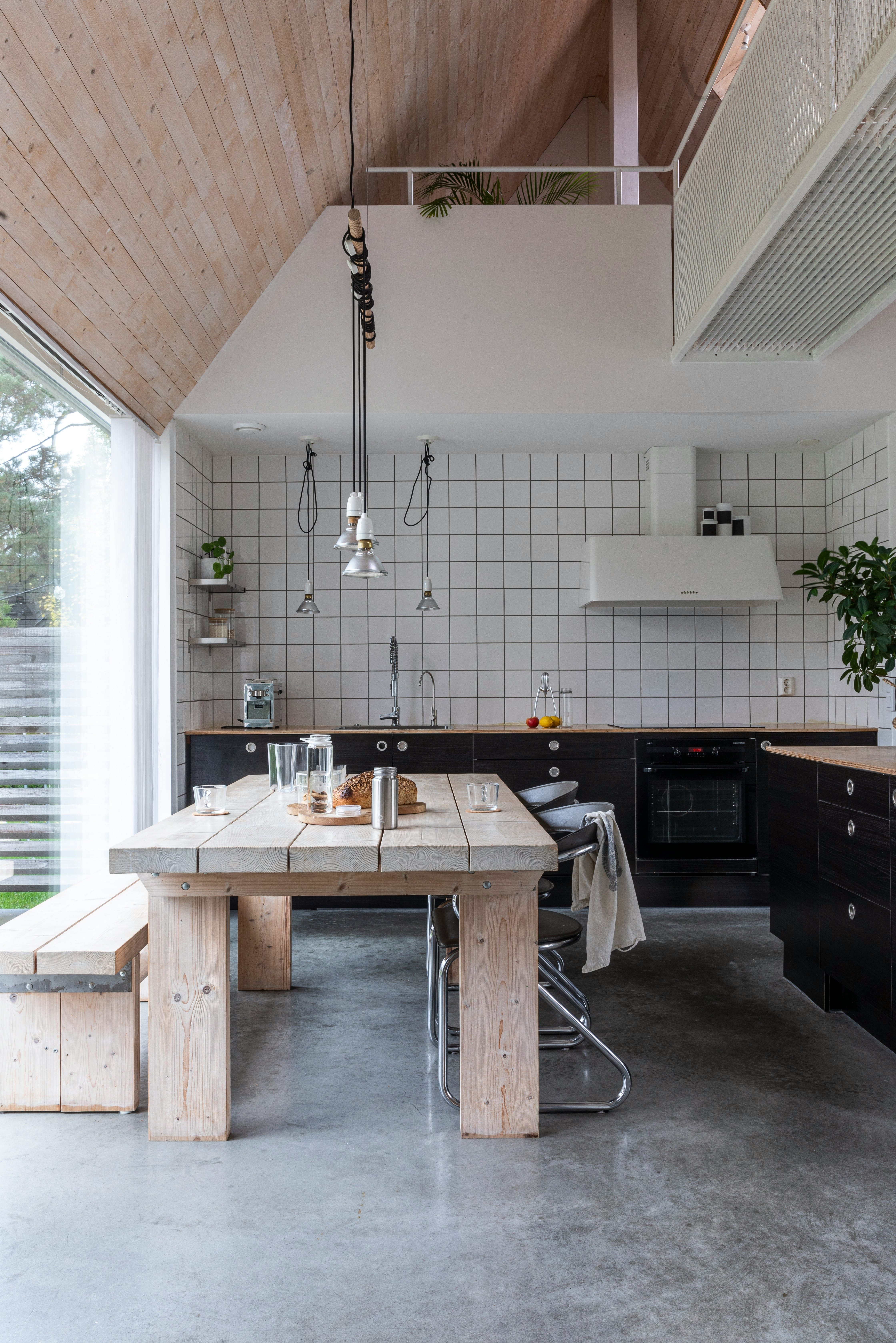 Vaulted kitchen with a wooden dining table, loaf of bread on a board, water carafe, black cabinets, and white square tile backsplash